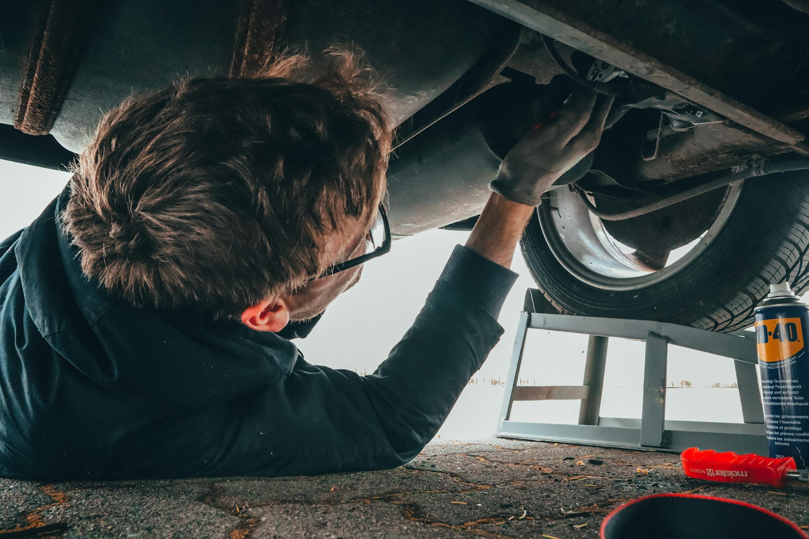 A man is working underneath a car, positioned near the wheels, focused on repairs.