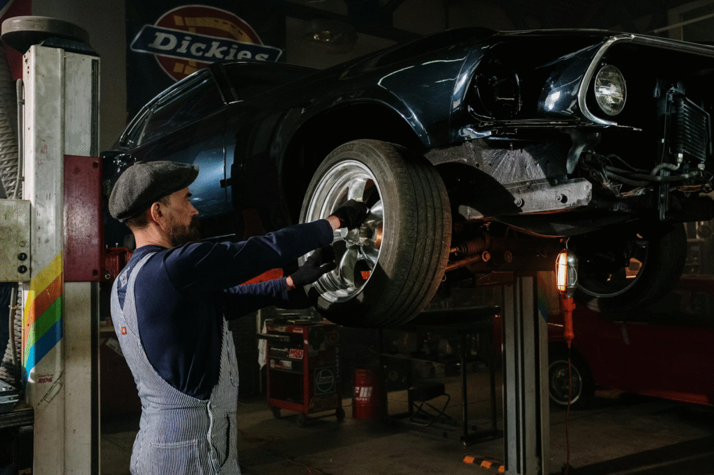 A man repairs a car in a well-lit garage, surrounded by tools and equipment.