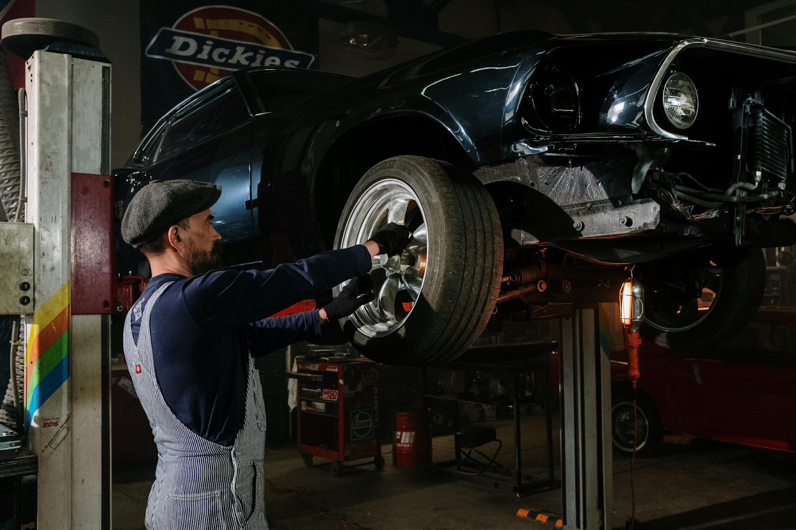 A man repairs a car in a well-lit garage, surrounded by tools and equipment.