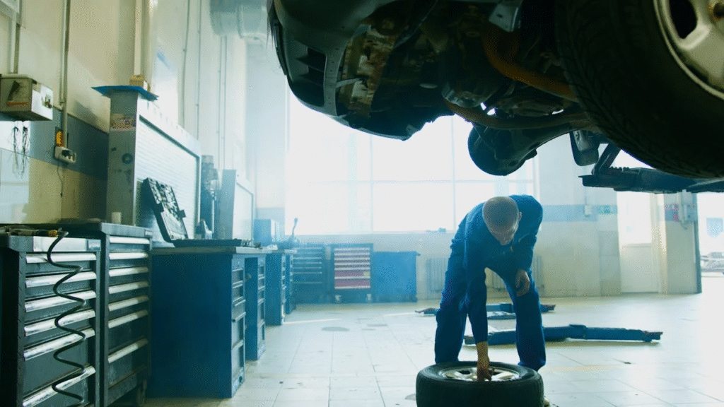 A man is working underneath a car, positioned near the wheels, focused on repairs.